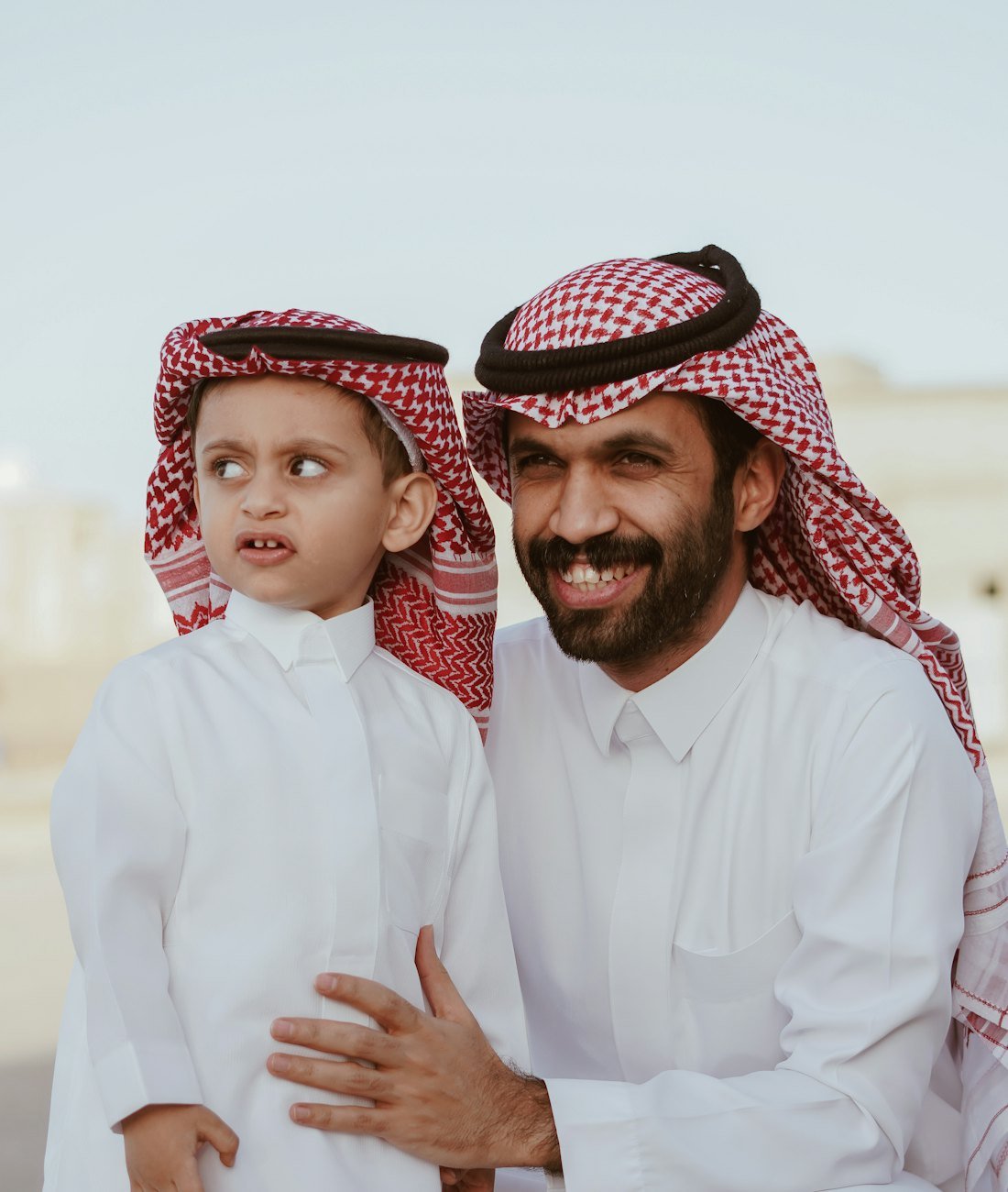 Emirati father and young son in traditional kandura and ghutra, smiling together